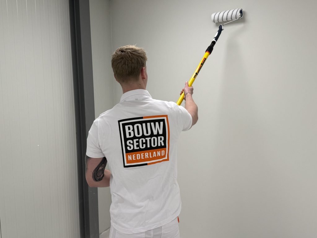 Schilder van Bouwsector Nederland rolt met een verlengsteel een lichte wand naast een deurkozijn